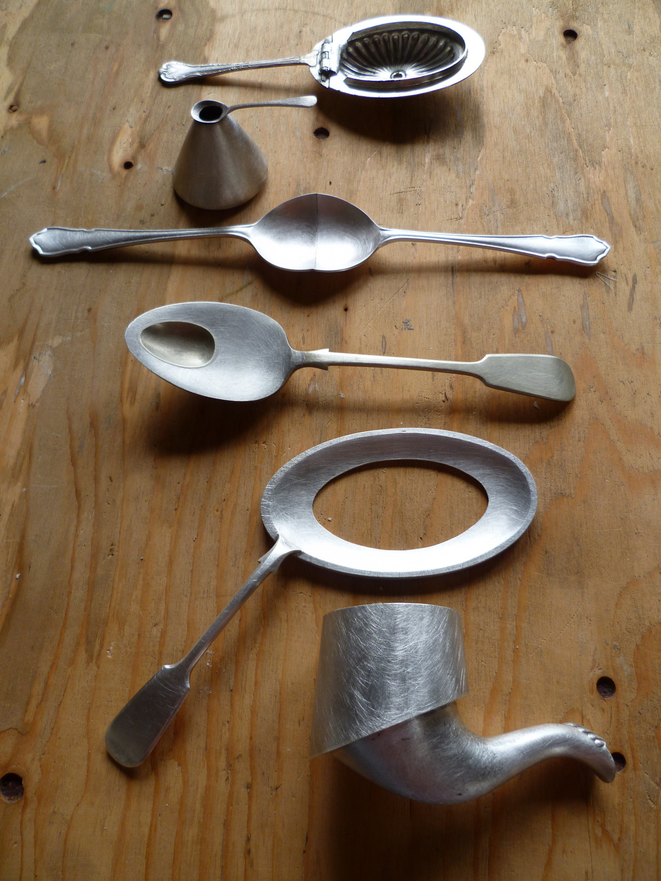 Image of a series of spoons that have been altered to indicate different use and function, laid out on a table.